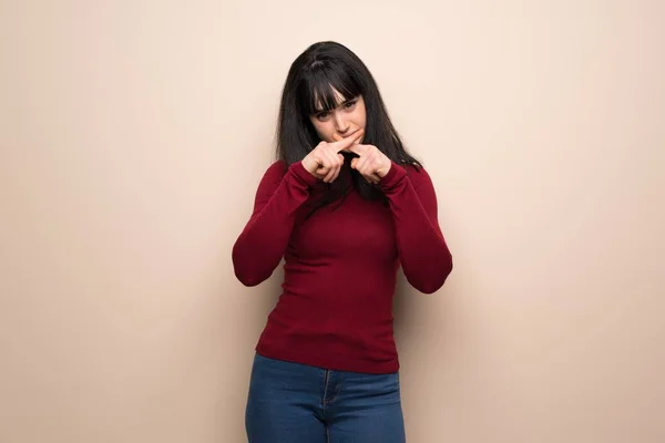 Young woman with red turtleneck showing a sign of silence gesture