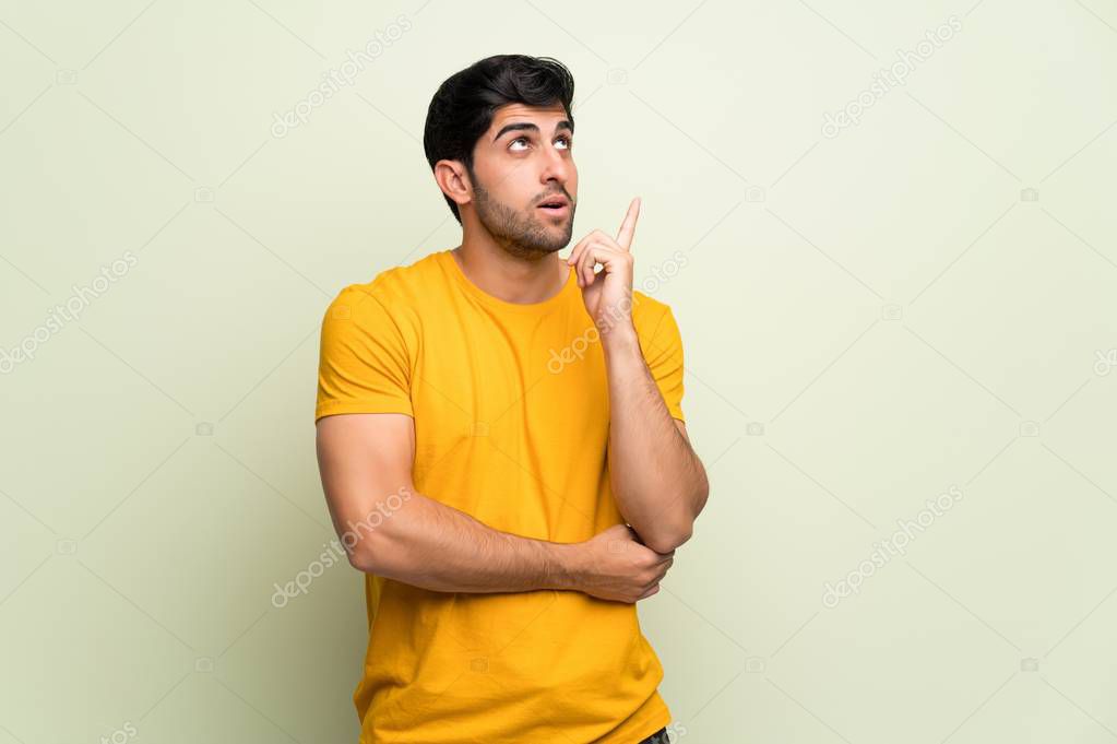 Young man over pink wall thinking an idea pointing the finger up