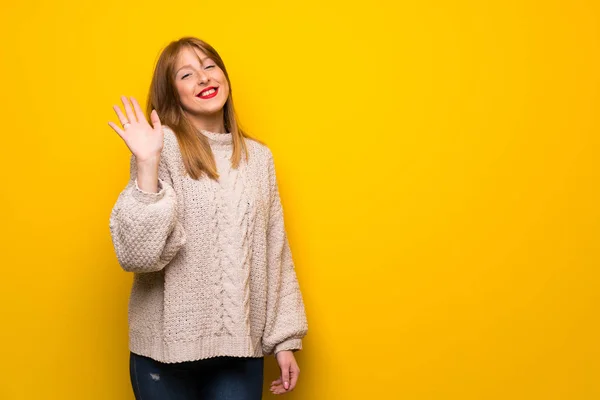 黄色の壁が幸せな表情で手で敬礼の赤毛の女性 — ストック写真