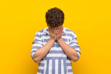 Sarışın adam yorgun ve hasta ifade ile sarı duvarın üzerinden