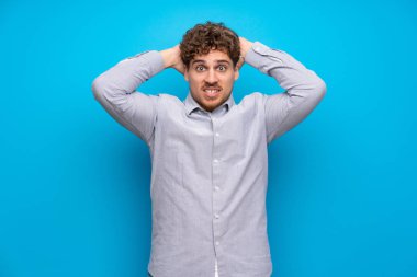 Mavi duvarın üzerinden sarışın adam sinirli ve ellerini başının üstüne alır