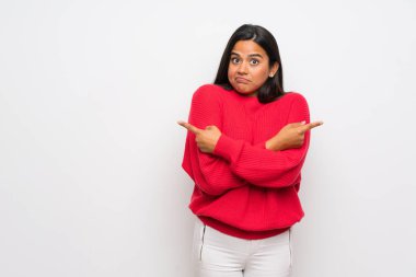 Young Colombian girl with red sweater pointing to the laterals having doubts clipart