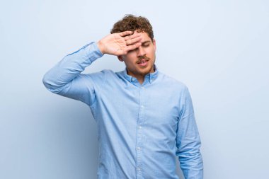 Sarışın adam yorgun ve hasta ifade ile mavi duvarın üzerinden