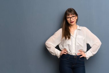 Mavi duvara gözlük ile kadın kalça kollar ile poz ve ön görünümlü gülüyor