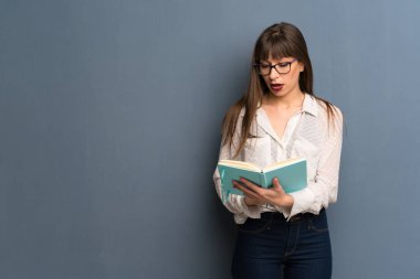 Bir kitap okuma tadını çıkarırken mavi duvar üzerinde gözlük ile kadın şaşırttı