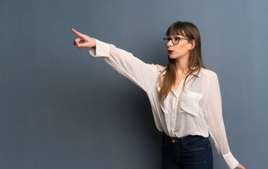 Mavi duvara bakan gözlük ile kadın uzağa işaret