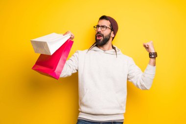 Zafer pozisyonunda alışveriş çantaları bir sürü tutan dreadlocks ile hippi adam