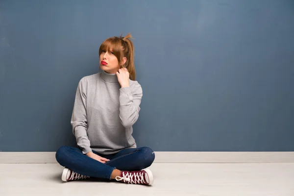 Redhead woman siting on the floor with tired and sick expression