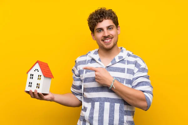 Hombre Rubio Sobre Pared Amarilla Sosteniendo Una Casita —  Fotos de Stock