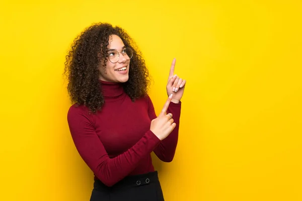 Dominican woman with turtleneck sweater pointing with the index finger and looking up