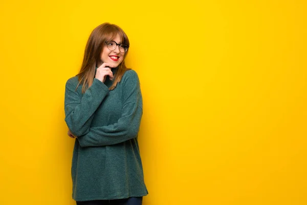 Kobieta Okularach Żółty Ścianę Patrząc Bok Ręką Brodzie — Zdjęcie stockowe