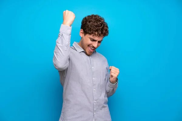 Hombre Rubio Sobre Pared Azul Celebrando Una Victoria —  Fotos de Stock