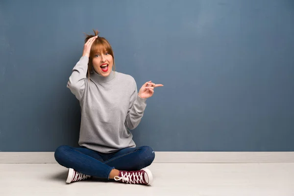 Rothaarige Frau Sitzt Überrascht Auf Dem Boden Und Zeigt Mit — Stockfoto