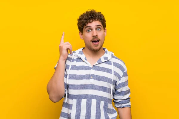 Homem Loiro Sobre Parede Amarela Pensando Uma Ideia Apontando Dedo — Fotografia de Stock