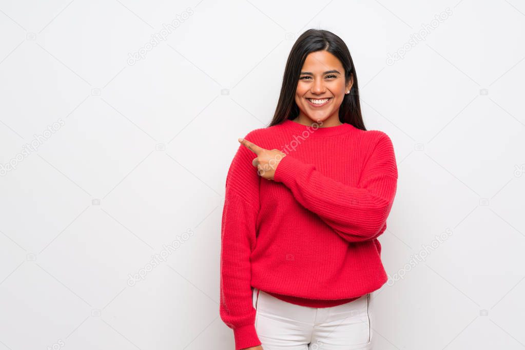 Young Colombian girl with red sweater pointing to the side to present a product