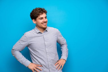 Sarışın adam silah, kalça ile poz ve gülümseyen mavi duvarın üzerinden