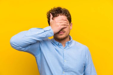 Sarışın adam izole sarı duvar eller tarafından gözleri kaplama