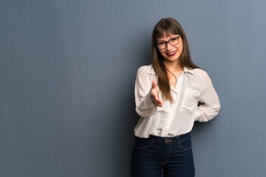 İyi bir anlaşma kapanış için eller sallayarak mavi duvar üzerinde gözlük ile kadın