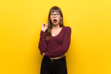 Woman with glasses over yellow wall thinking an idea pointing the finger up clipart
