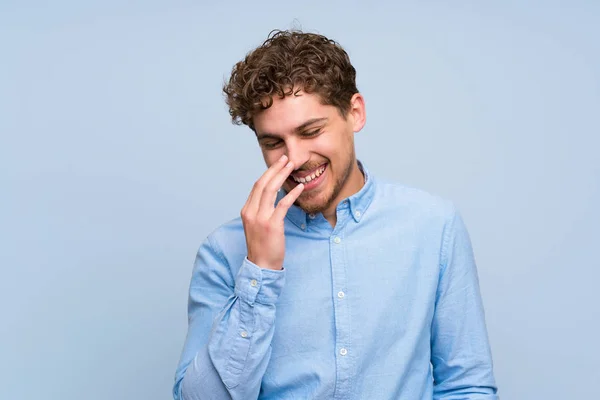 Blonde man over blue wall smiling a lot