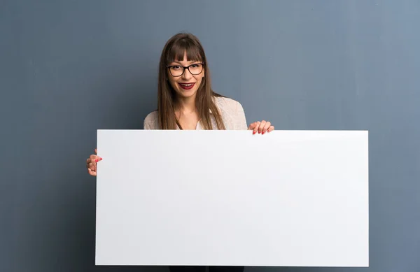 戴眼镜在蓝色墙上的妇女拿着一个空标语牌插入一个概念 — 图库照片