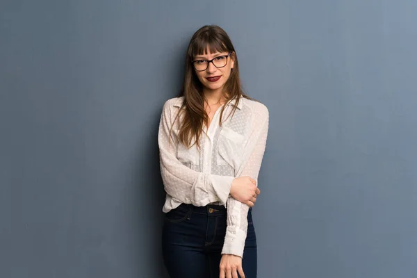 Woman with glasses over blue wall smiling