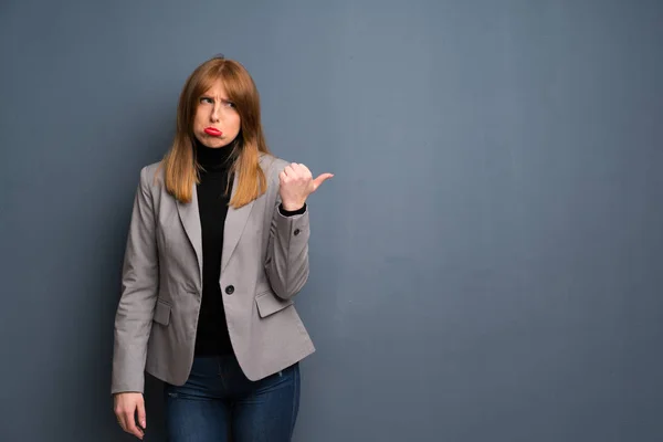 Redhead business woman unhappy and pointing to the side