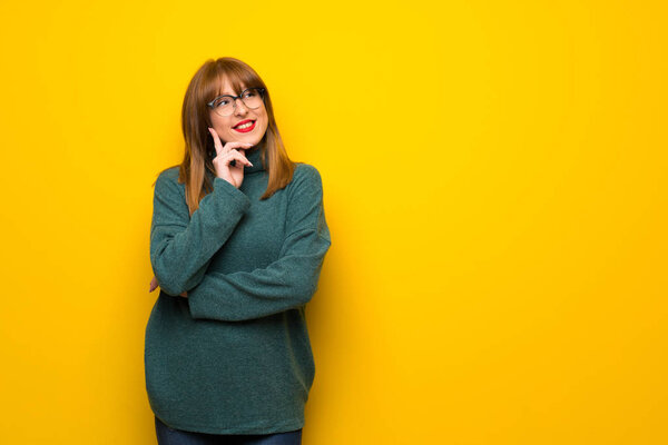 Woman with glasses over yellow wall thinking an idea while looking up