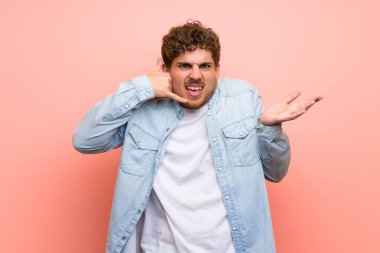 Sarışın adam şaşırttı ve telefon jest yapma pembe duvar üzerinde