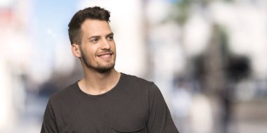 Siyah gömlek açık havada önüne bakarak gülen adam