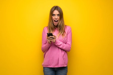 Kadın pembe kazaklı şaşırttı ve ileti gönderme sarı duvarın üzerinden