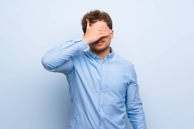 Mavi duvar eller tarafından gözleri kaplama sarışın adam. Bir şey görmek istiyor musunuz