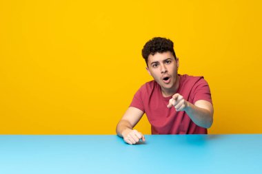 Renkli duvar ve masa şaşırmış ve işaretleme açık olan genç adam