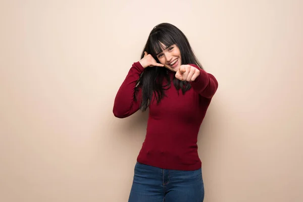 Young woman with red turtleneck making phone gesture and pointing front