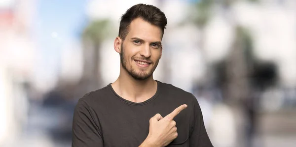 Man with black shirt pointing to the side to present a product at outdoors