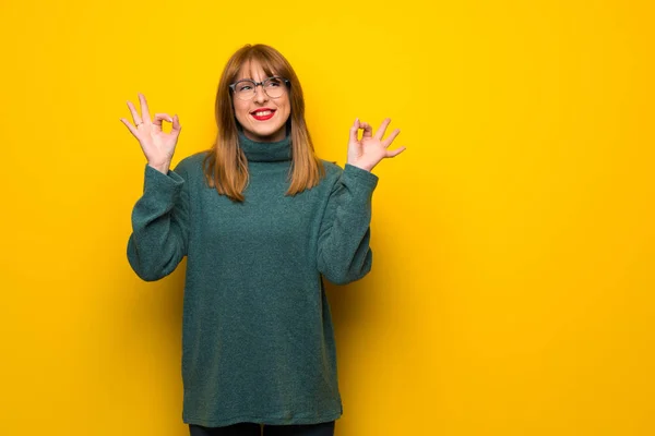 Woman with glasses over yellow wall in zen pose