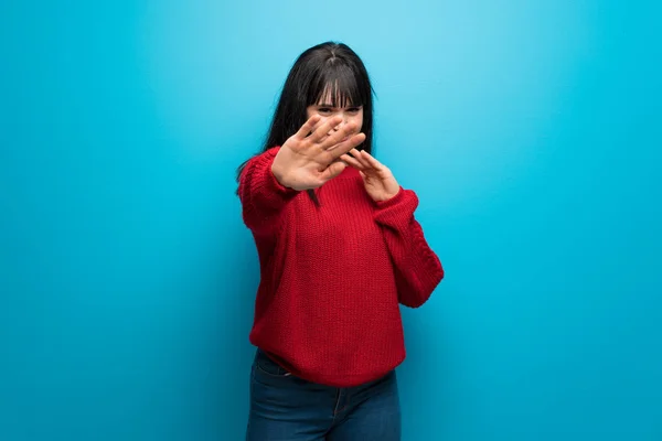 Woman with red sweater over blue wall nervous and scared stretching hands to the front