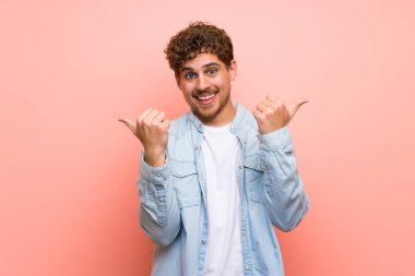 Her iki el ile jest Yaşasın vererek ve gülümseyen pembe duvar sarışın adam