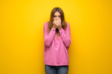 Sarı duvar üzerinde pembe kazak ile kadın, uygunsuz bir şey söyleyerek eller ile ağız kapsayan