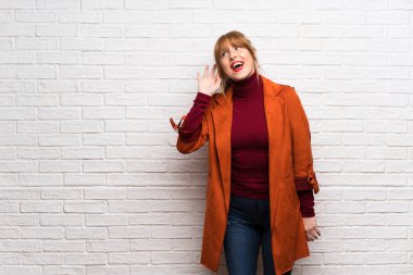 Kat bir şey kulak el koyarak dinleme beyaz tuğla duvarın üzerinden kadınla