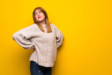 Kızıl saçlı kadın için bir çaba yapılmış olan sırt ağrısı muzdarip sarı duvarın üzerinden