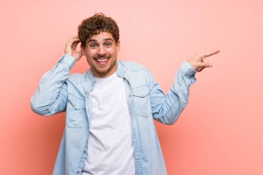 Sarışın adam parmak tarafına işaret ve bir ürün sunan pembe duvar üzerinde