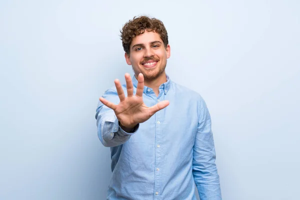 Blond Man Över Blå Vägg Räknar Fem Med Fingrar — Stockfoto