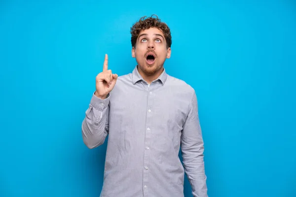 Hombre Rubio Sobre Pared Azul Apuntando Hacia Arriba Sorprendido — Foto de Stock