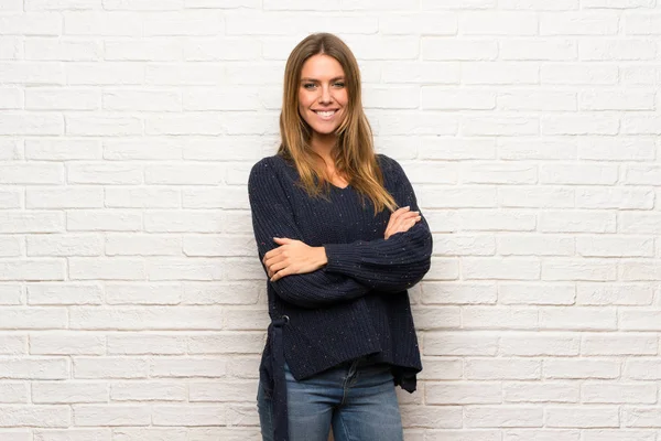 Blonde woman over brick wall with arms crossed and looking forward