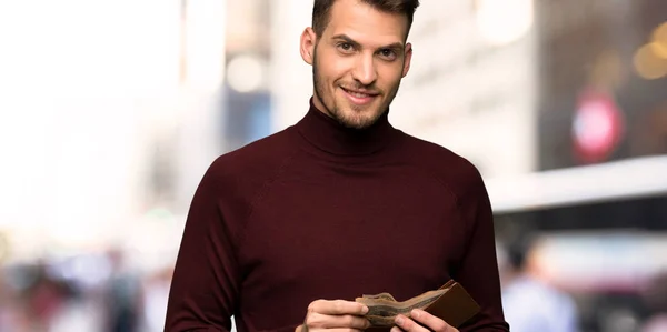 Man with turtleneck sweater holding a wallet in the city