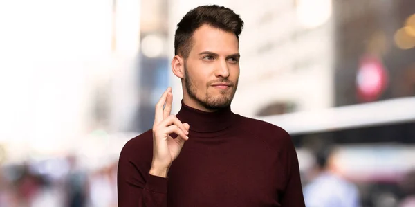 Man with turtleneck sweater with fingers crossing and wishing the best in the city