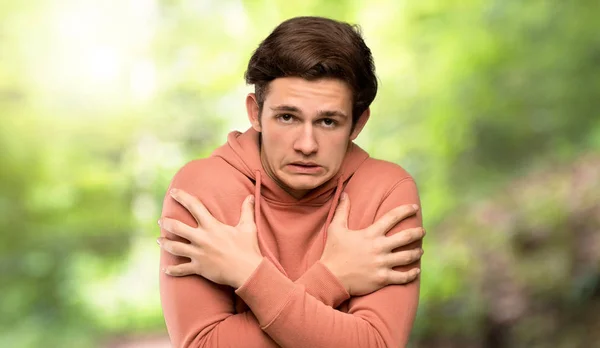 Teenager man with sweatshirt freezing at outdoors