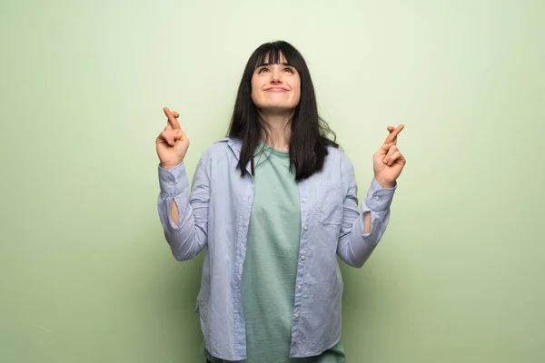 Young woman over green wall with fingers crossing and wishing the best