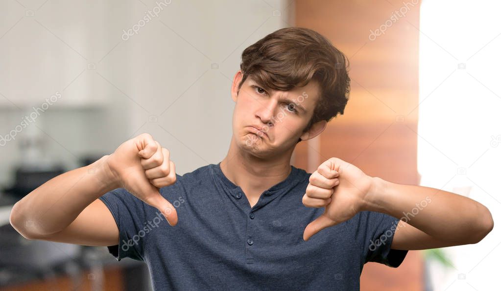 Teenager man showing thumb down at indoors